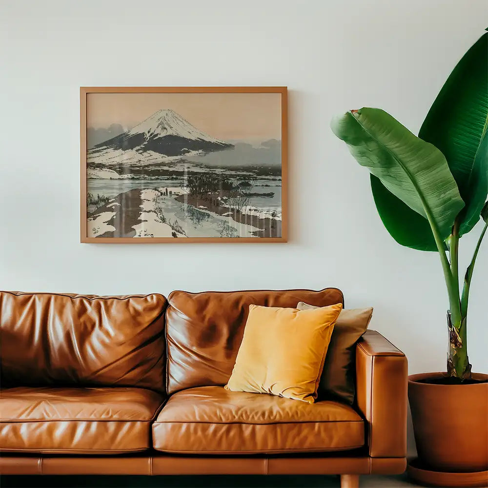 Framed painting of a snowy mountain landscape hanging above a brown leather couch with colorful cushions and a large potted plant.