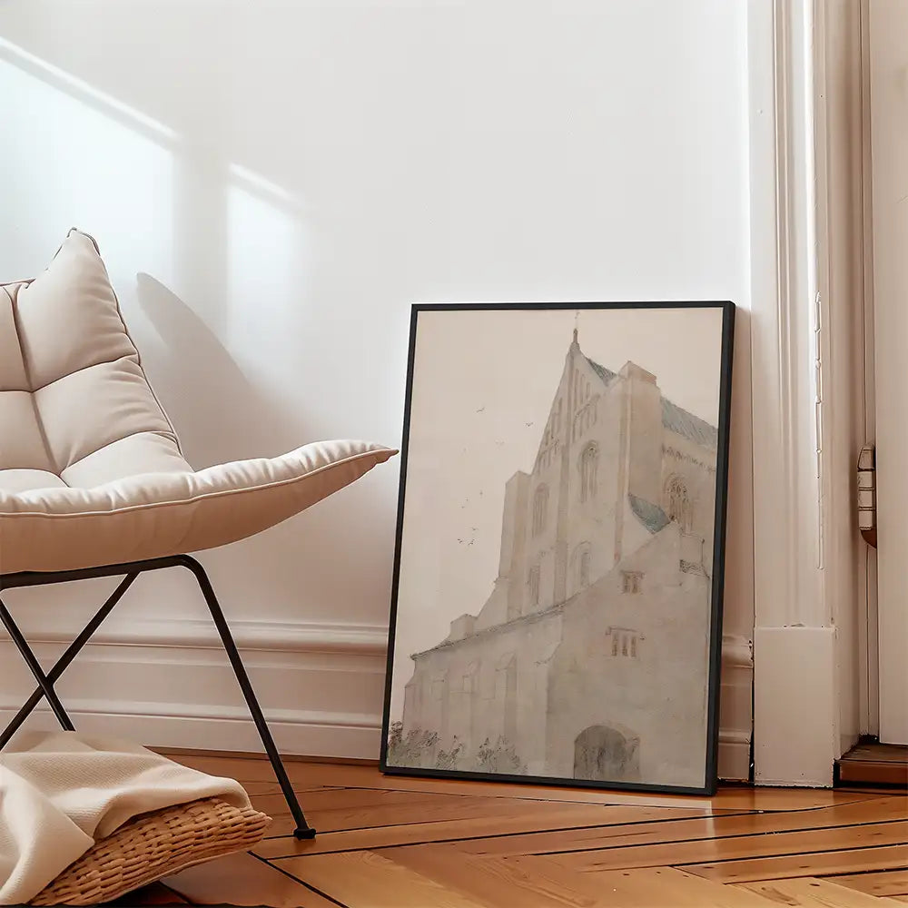 Framed watercolor painting of a historical building leaning against a wall next to a modern chair in a bright, minimalist interior.