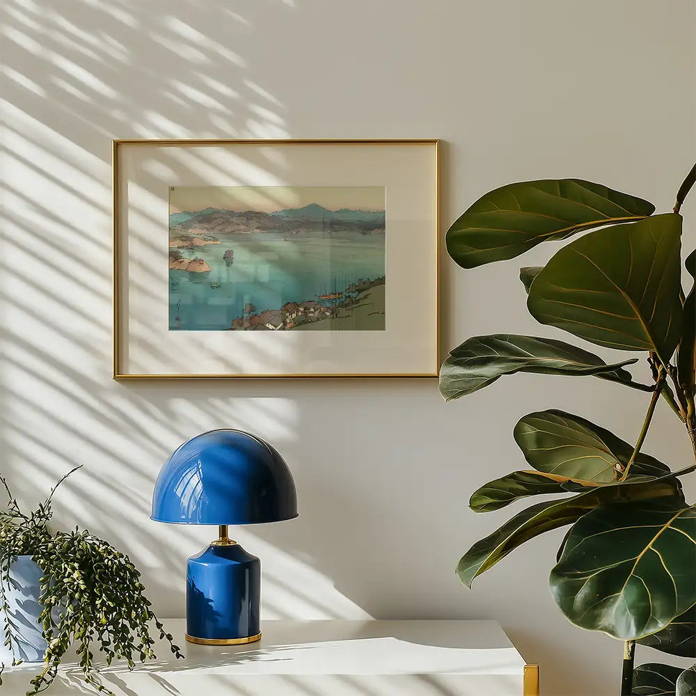 Framed painting of a serene landscape with mountains and water, displayed on a wall next to a blue lamp and a potted plant.