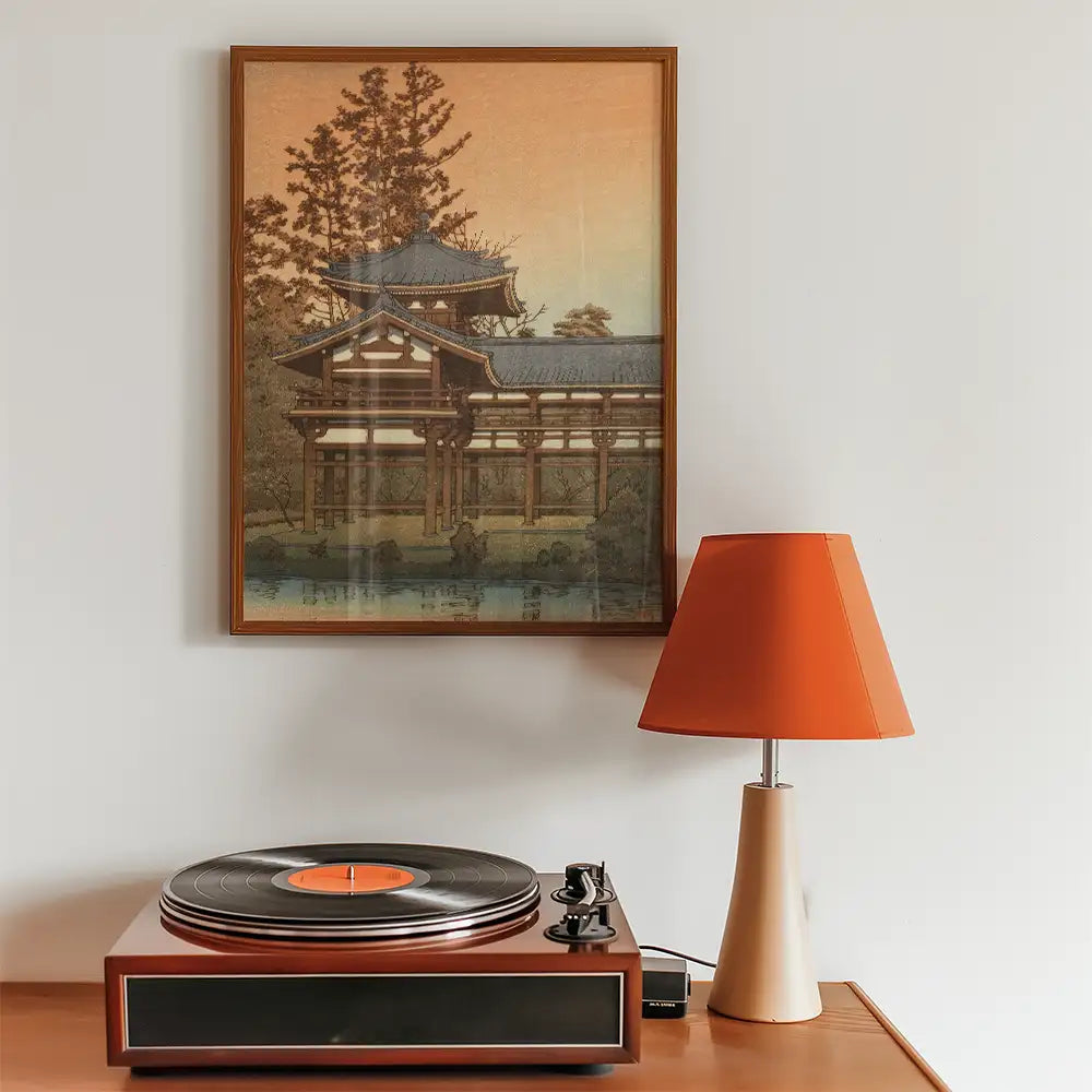 Framed painting of a traditional Japanese building with a serene landscape background, displayed above a vintage record player and a modern orange lamp.