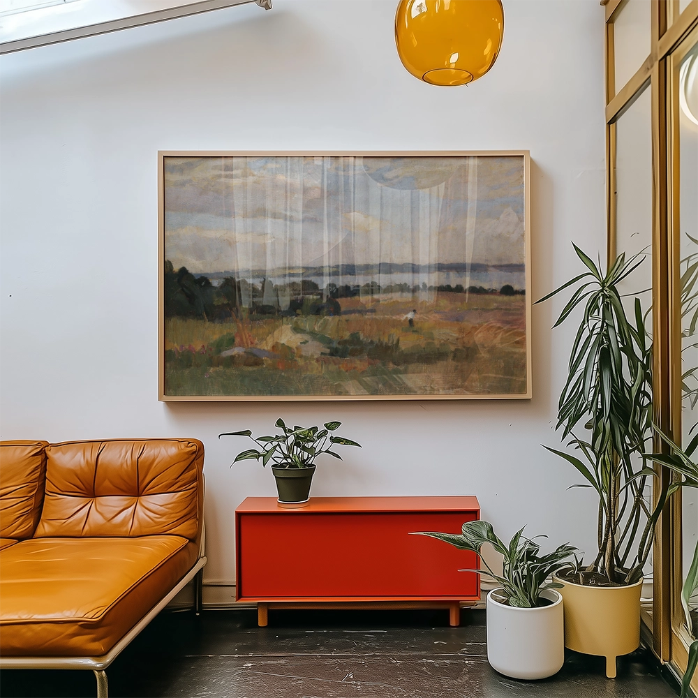 A framed landscape painting hanging above a red cabinet in a modern living room setting, with an orange couch and potted plants.