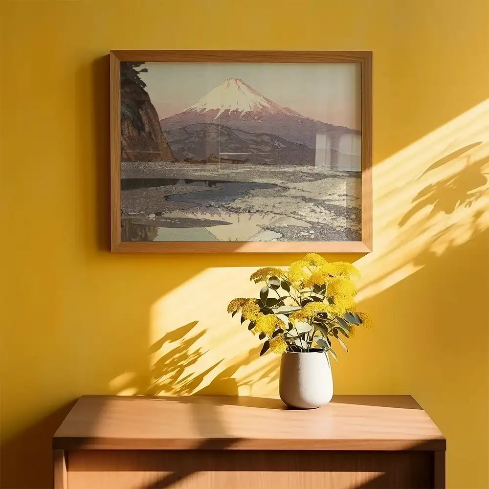 Framed painting of Mount Fuji against a yellow wall with a vase of yellow flowers on a wooden table.