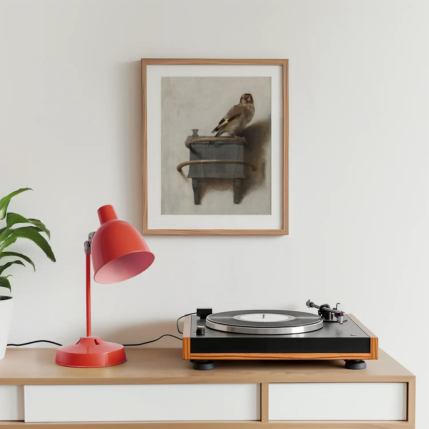 Framed painting of a bird perched on a container, displayed on a wall above a wooden table with a red lamp and a record player.
