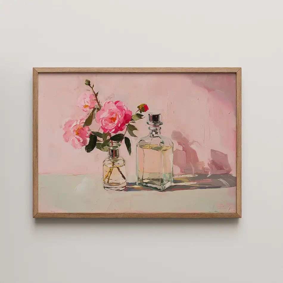 Framed painting of pink roses in a glass vase alongside two elegant glass perfume bottles against a soft pink background.