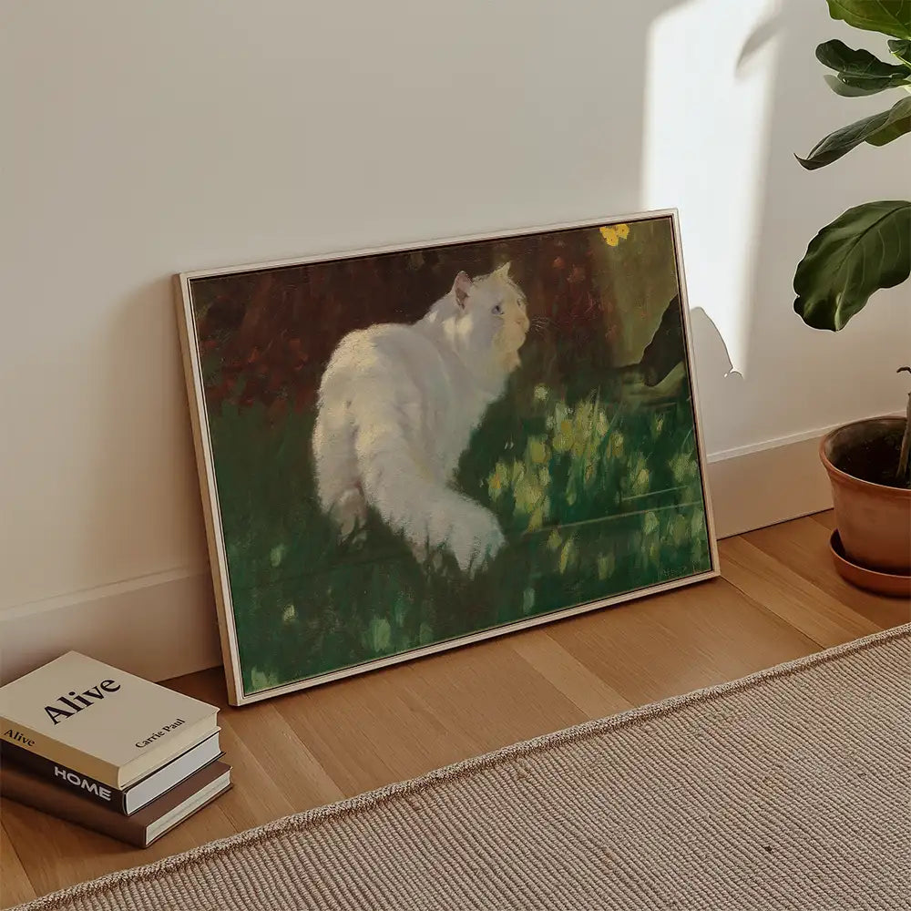 A framed painting of a white cat sitting in a field of yellow flowers, leaning against a wall with a plant and books in the foreground.