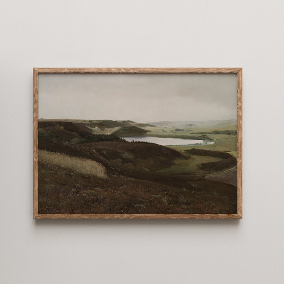 Framed landscape painting of rolling hills and a serene lake under a cloudy sky