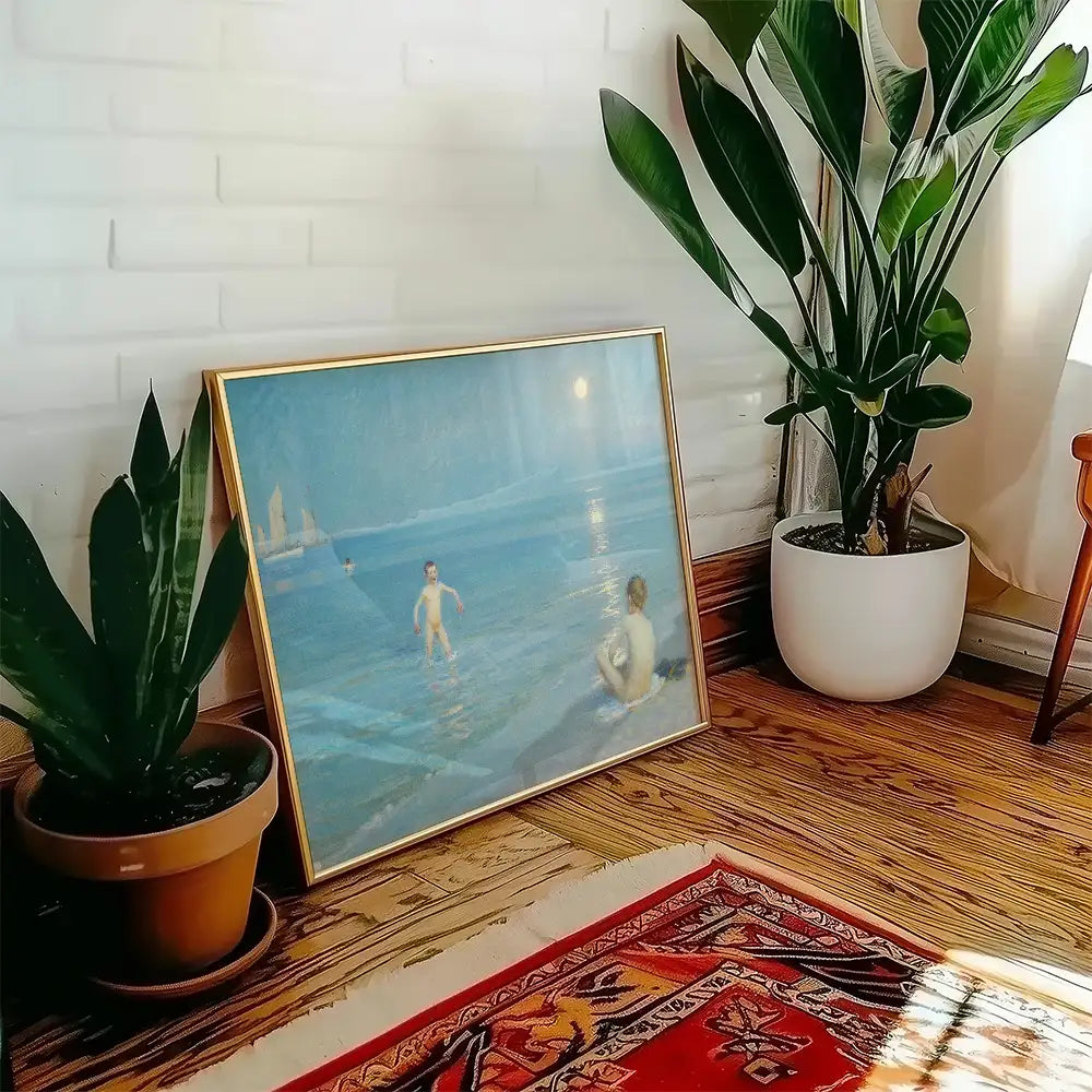 Painting of children playing by the water, framed in gold, displayed beside a potted plant in a cozy interior setting.
