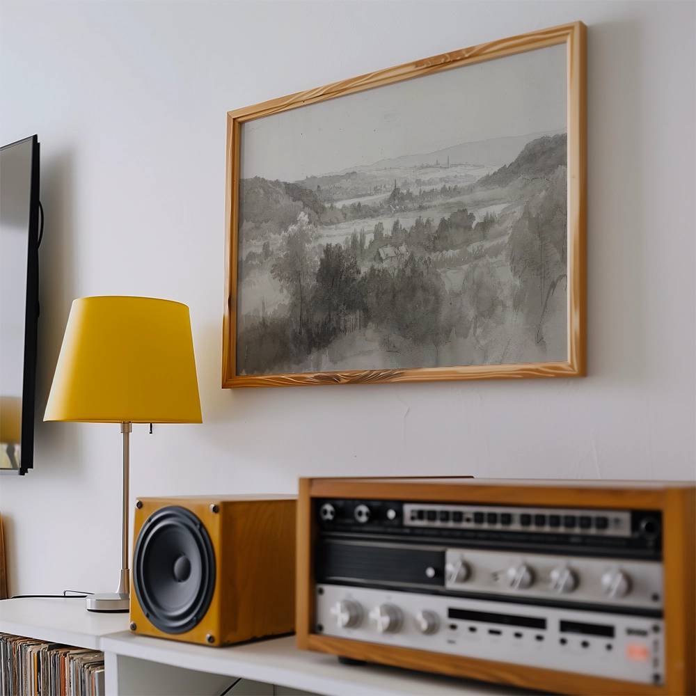 A framed black and white landscape painting hanging on a wall next to a yellow lamp and a vintage audio system.