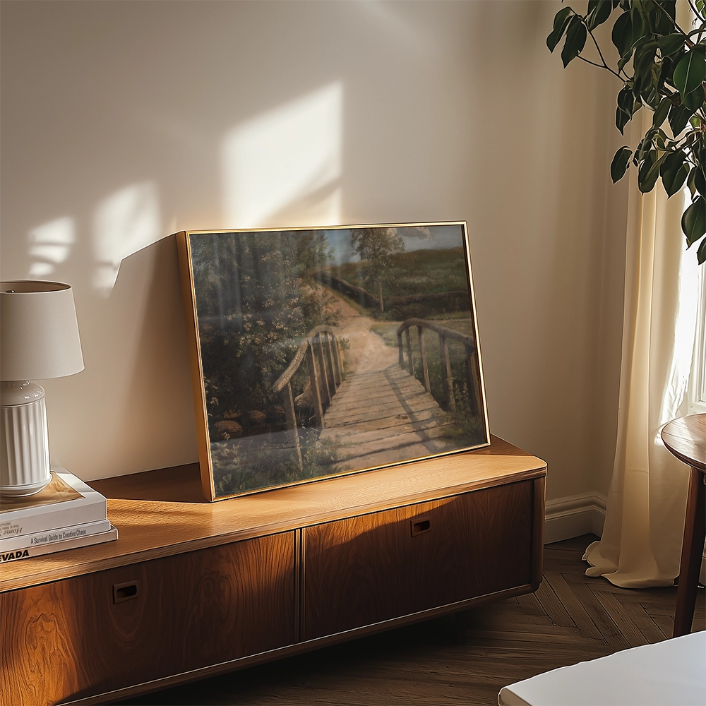 A framed painting of a tranquil landscape featuring a wooden bridge, greenery, and soft natural lighting, displayed on a wooden console table.