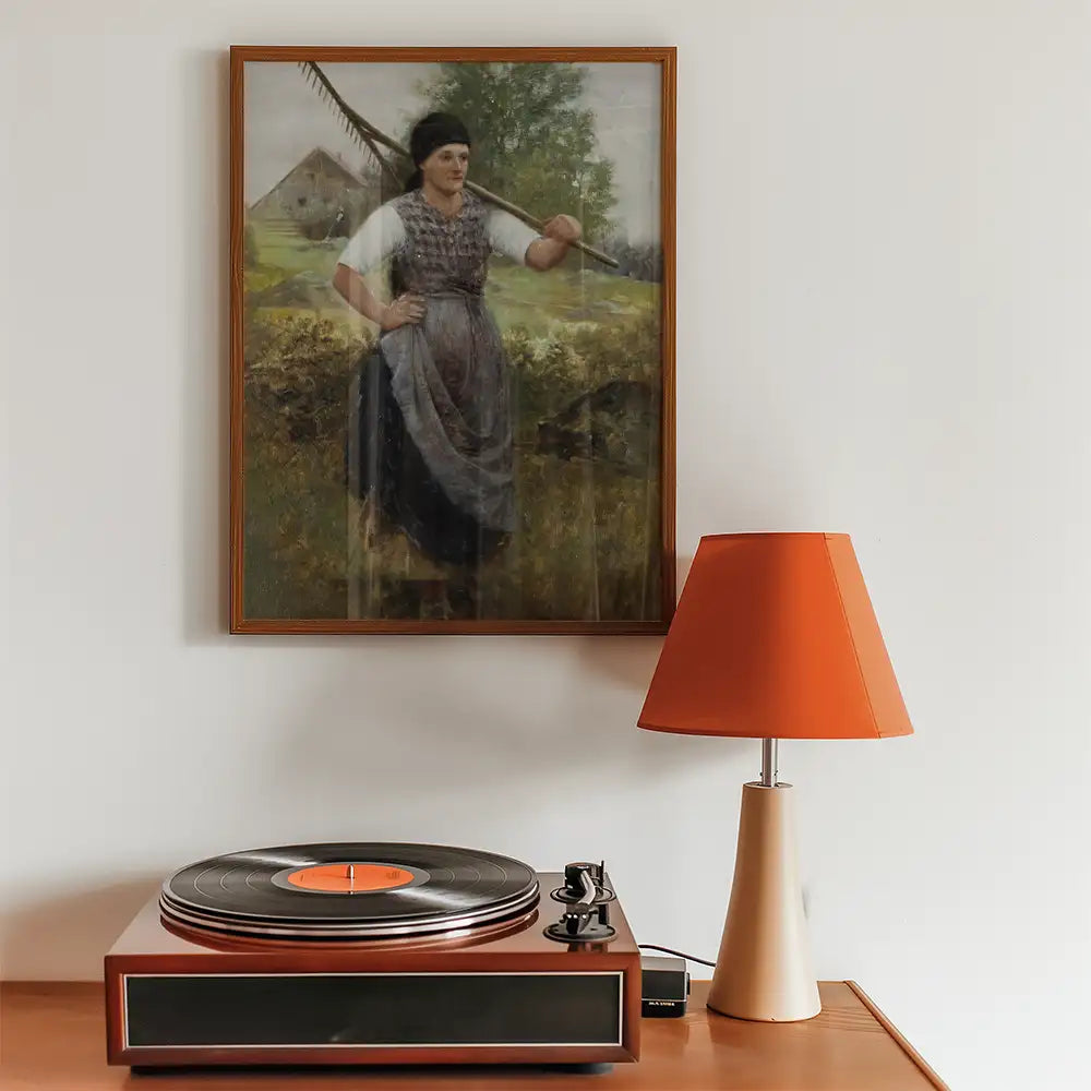 Framed painting of a woman holding a scythe outdoors, displayed above a vintage record player and an orange lamp.