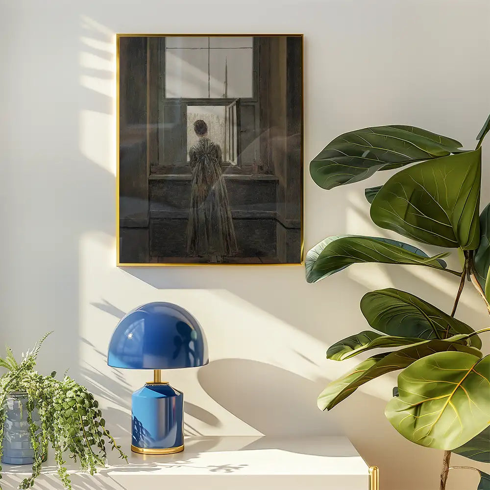 Painting of a woman in a long dress gazing out of an open window, framed in gold, displayed in a modern interior setting with a blue lamp and plants.
