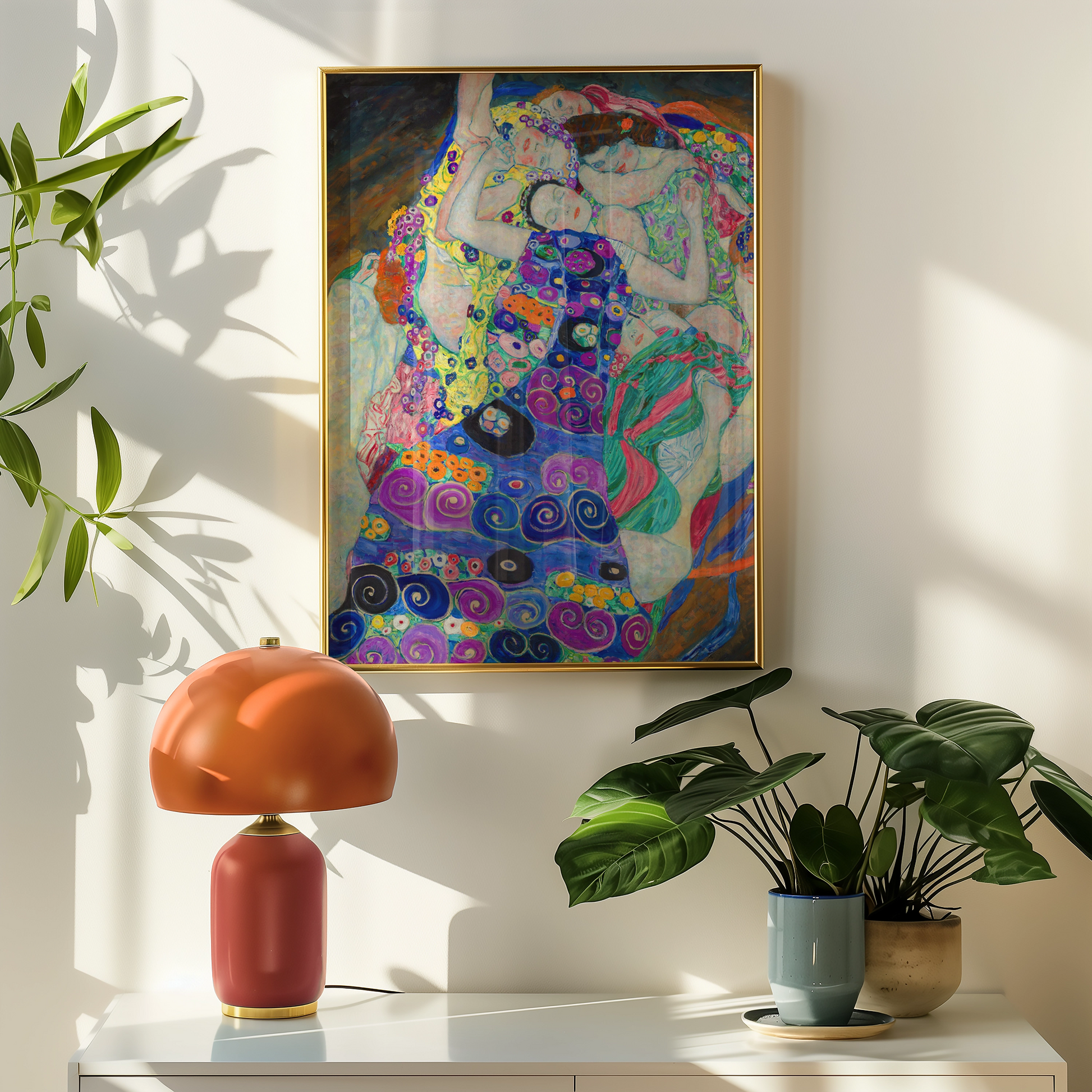 Colorful painting of figures embracing, framed and displayed on a wall above a stylish lamp and indoor plants.