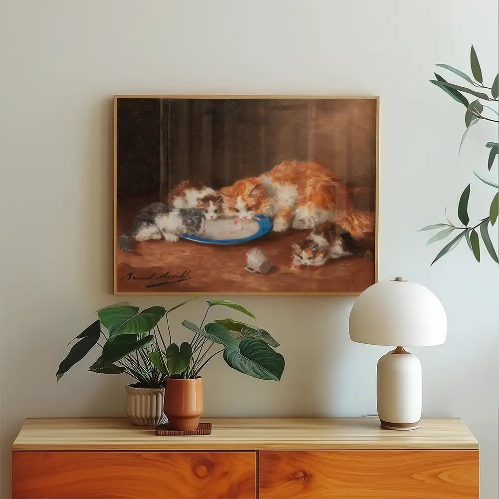 Painting of three kittens drinking from a blue plate, framed, displayed above a wooden cabinet with potted plants and a lamp.