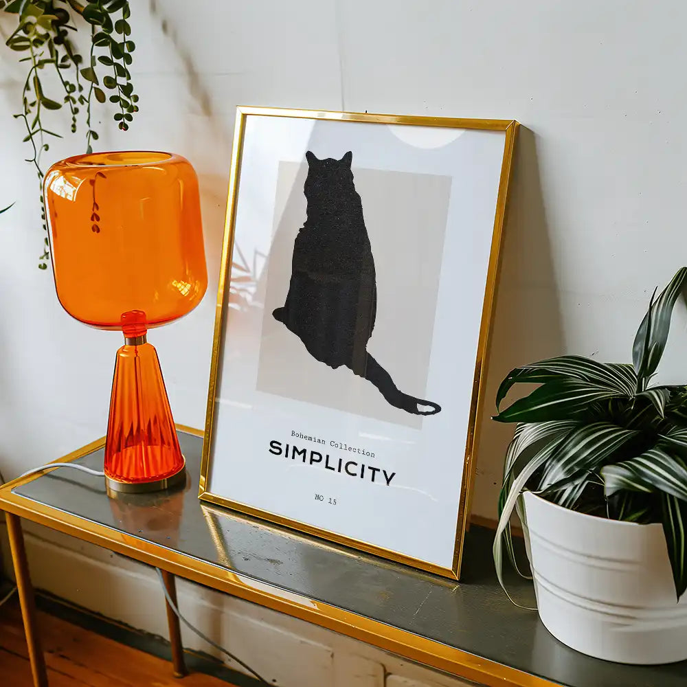 Modern poster art featuring a silhouetted cat, framed in gold, accompanied by a vibrant orange lamp and greenery, perfect for home decor.