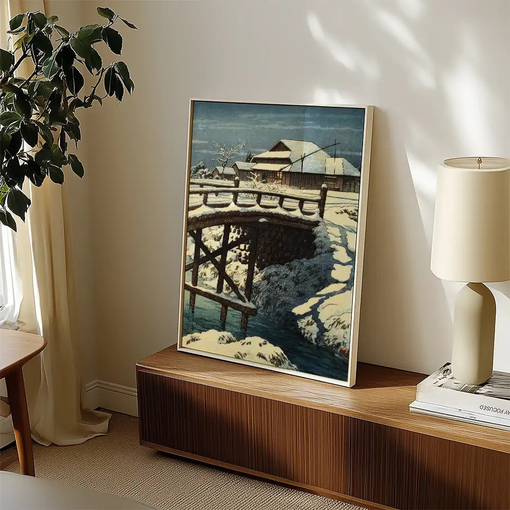 Framed painting of a snow-covered bridge and house displayed in a cozy living room setting.