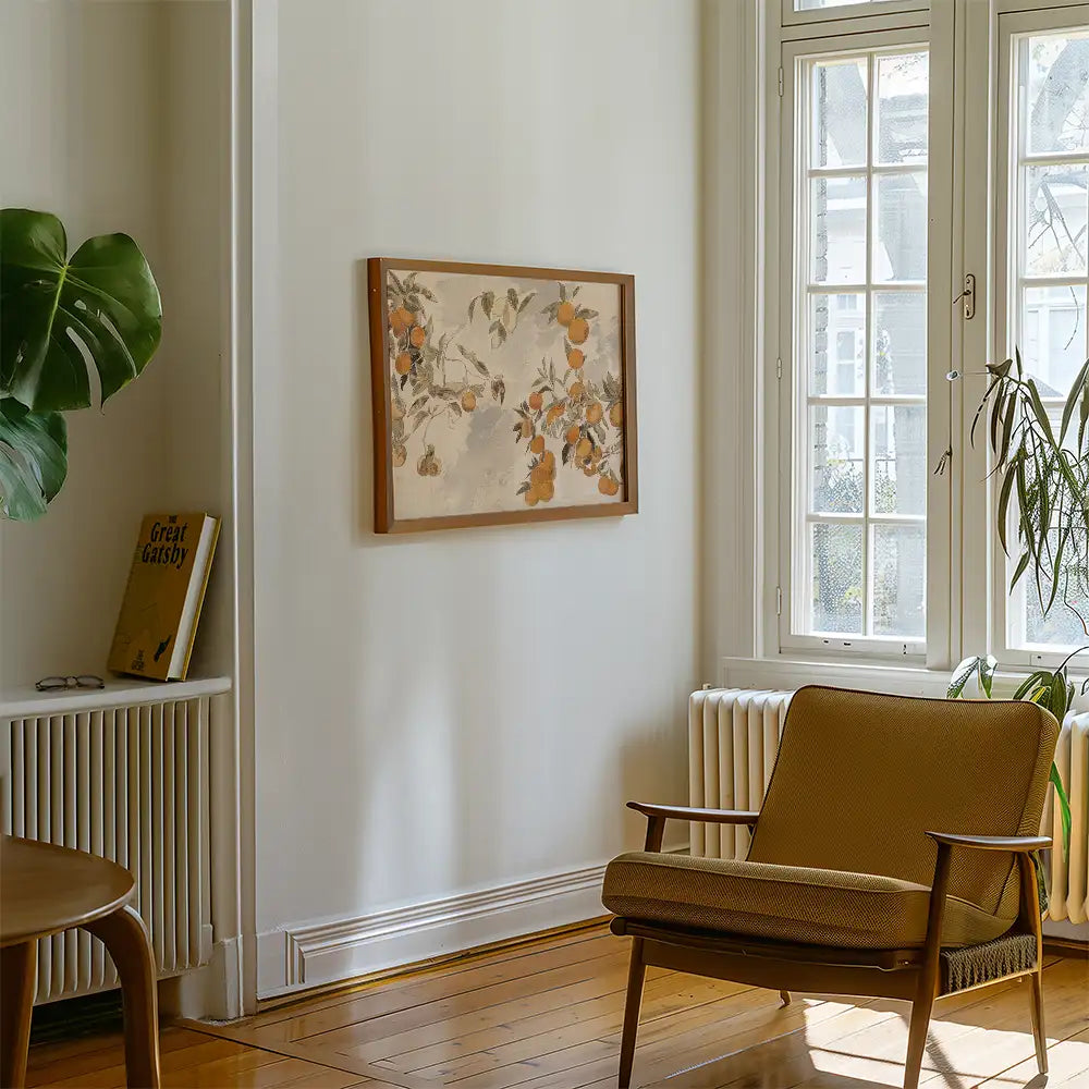 Painting featuring orange blossoms in a wooden frame, displayed on a light wall next to a green plant and an armchair in a cozy living space.