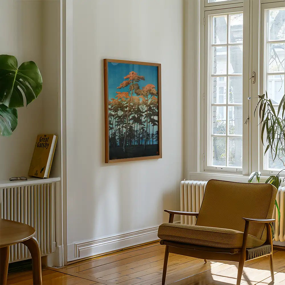 Framed painting of trees against a blue background, displayed on a white wall in a cozy living room with a brown armchair and a green plant.