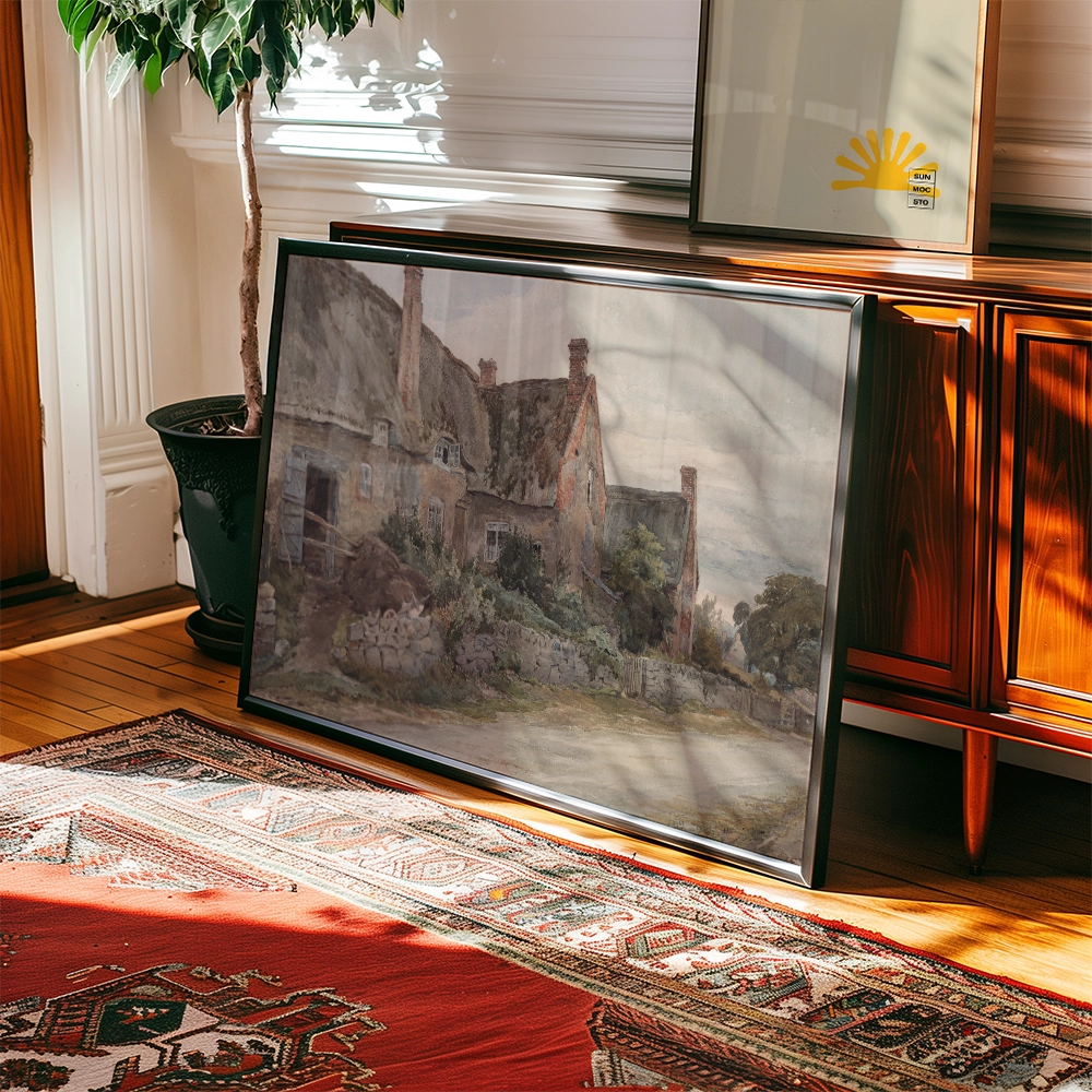 Framed watercolor painting of a countryside cottage resting on a wooden floor next to a decorative plant and a wooden cabinet.