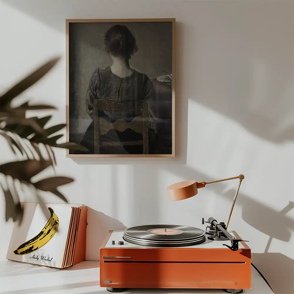 A vintage painting of a woman seen from the back, hanging above an orange turntable with a record player and a banana-themed vinyl cover on display.