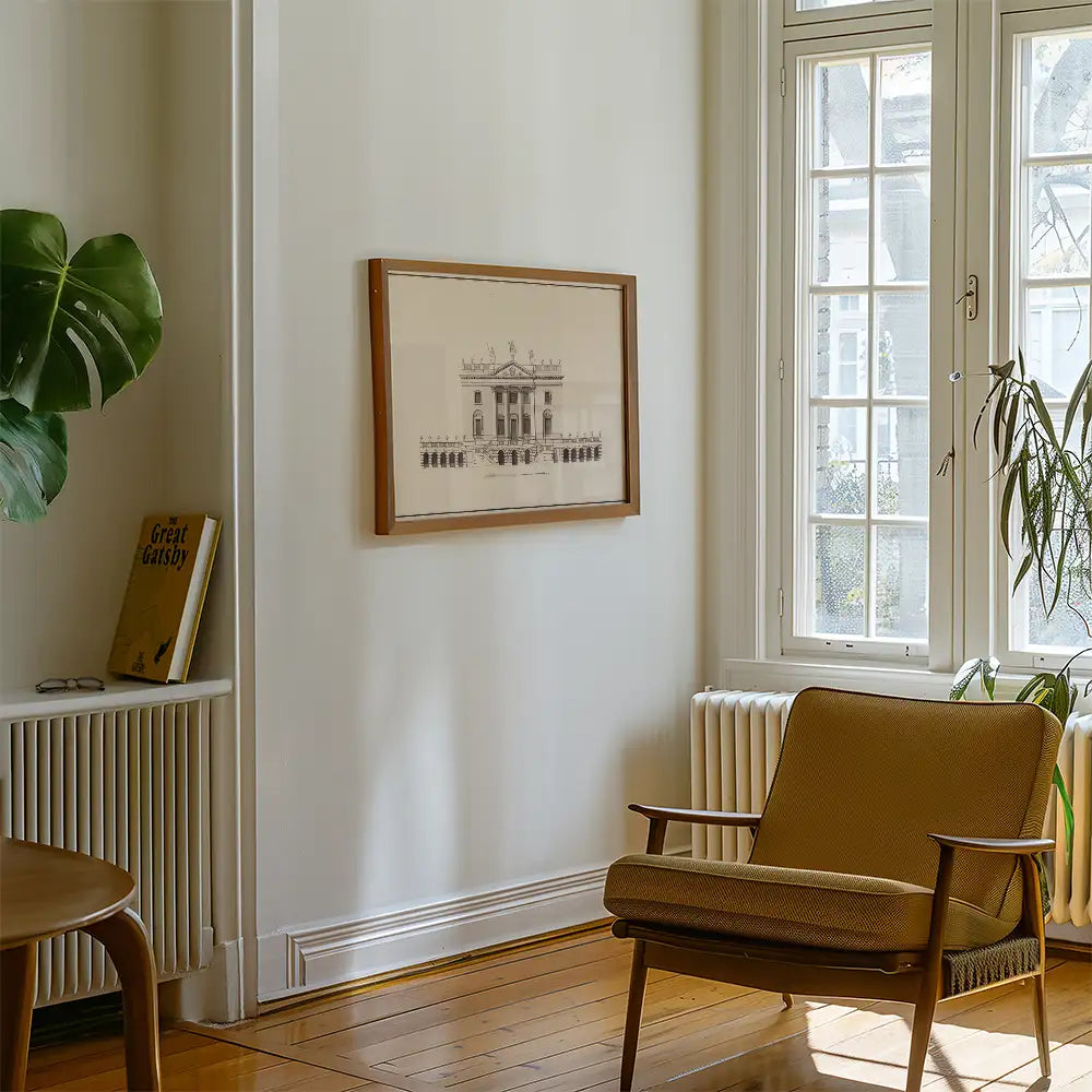 Framed architectural print hanging on a wall in a cozy living room with a plant and a wooden chair.