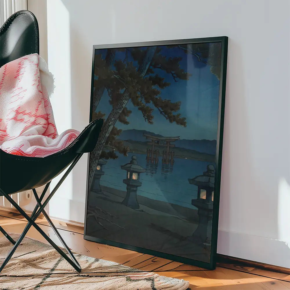 Framed painting of a tranquil lakeside scene with lanterns and a torii gate, leaning against a wall next to a stylish chair and blanket.