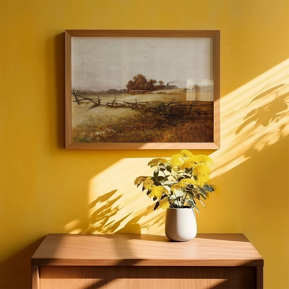 Framed landscape painting on a yellow wall above a wooden side table with a vase of yellow flowers.