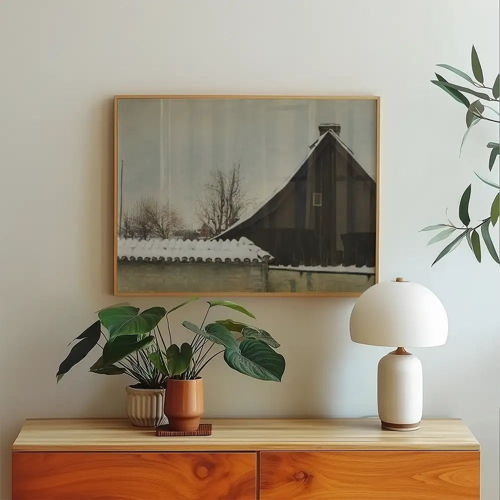 Framed painting of a snow-covered house with bare trees, displayed above a wooden side table with decorative plants and a lamp.