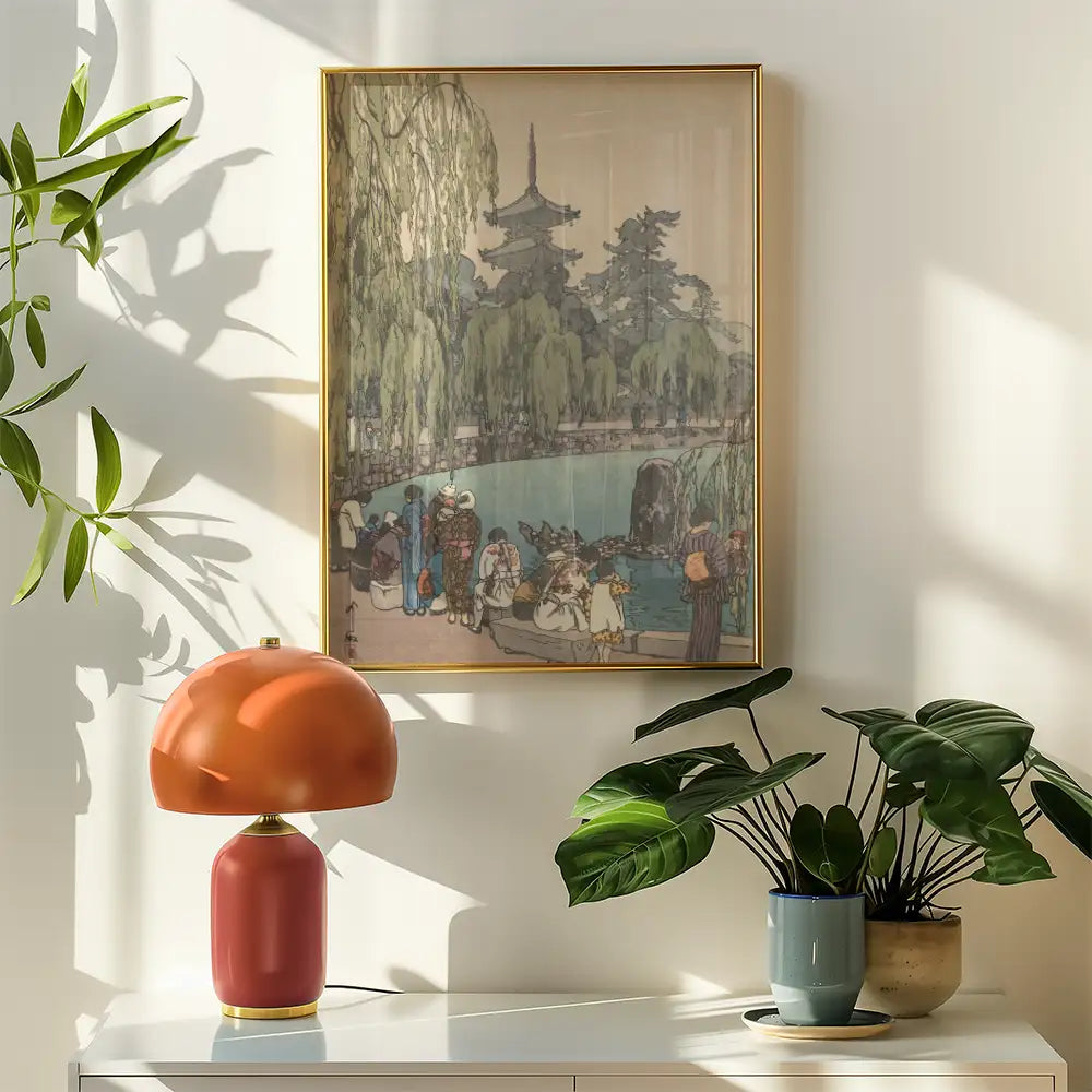 Framed painting depicting a serene outdoor scene with people by a pond, surrounded by trees, complemented by a stylish lamp and potted plants on a white shelf.