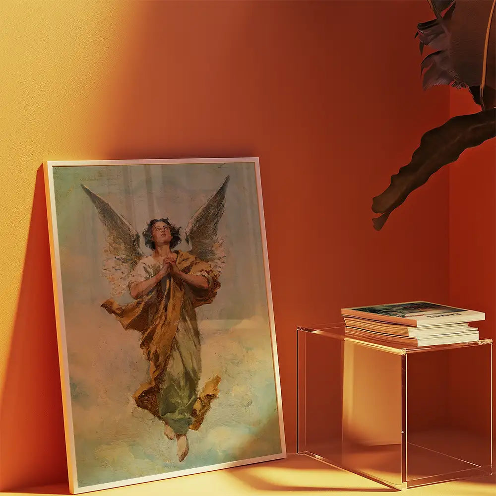 Framed painting of an angel with wings in a prayerful pose against an orange wall, accompanied by a stack of books on a clear acrylic table.