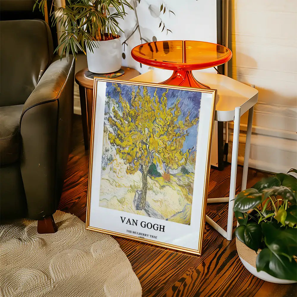 Van Gogh painting "The Mulberry Tree" displayed in a gold frame next to a plant and side table in a cozy living room setting.