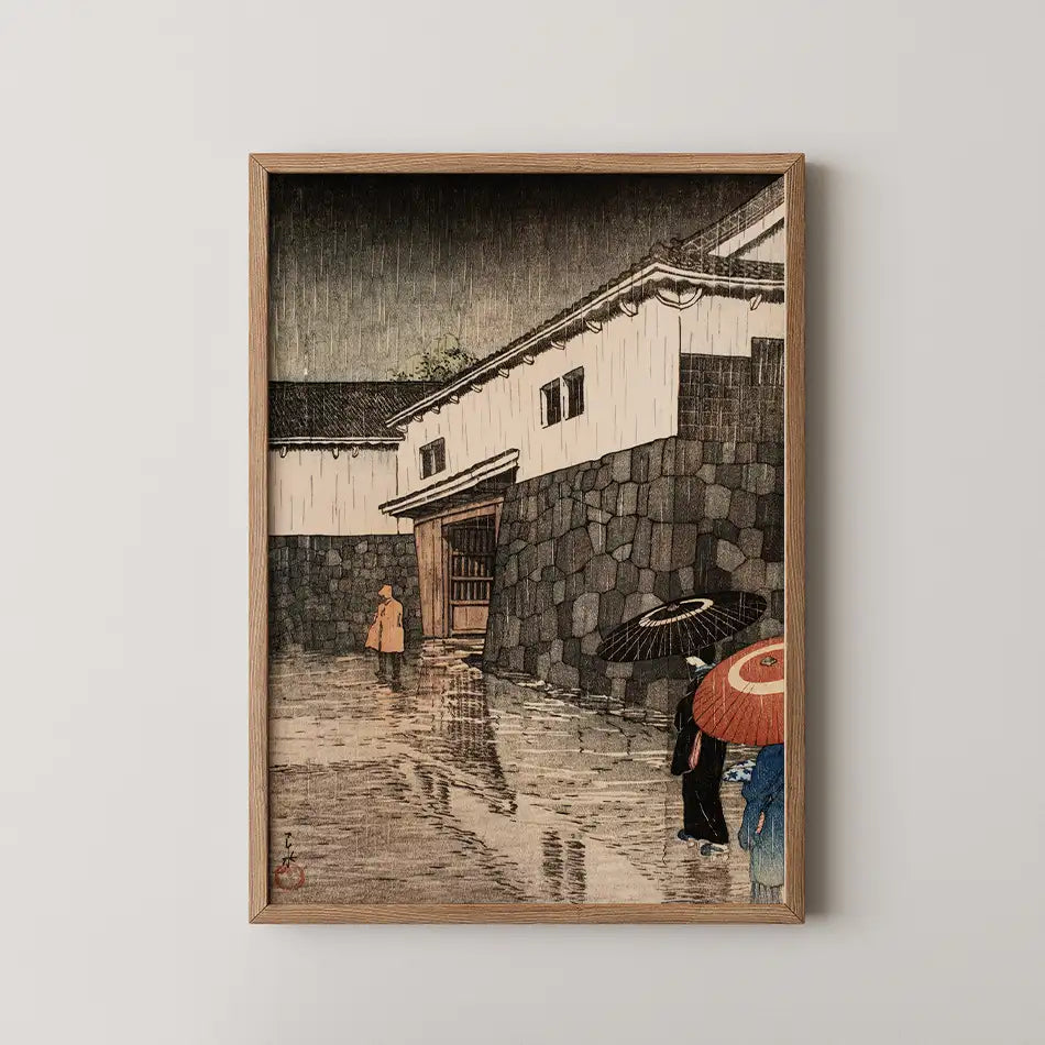 Framed painting of two figures with umbrellas walking on a rain-soaked street near a traditional building with a stone wall.