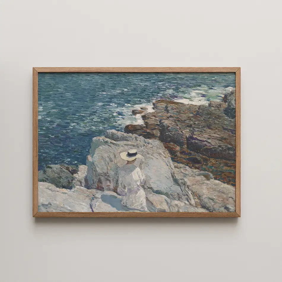 Painting of a figure in a white outfit and hat sitting on rocks by the sea, framed in wood.