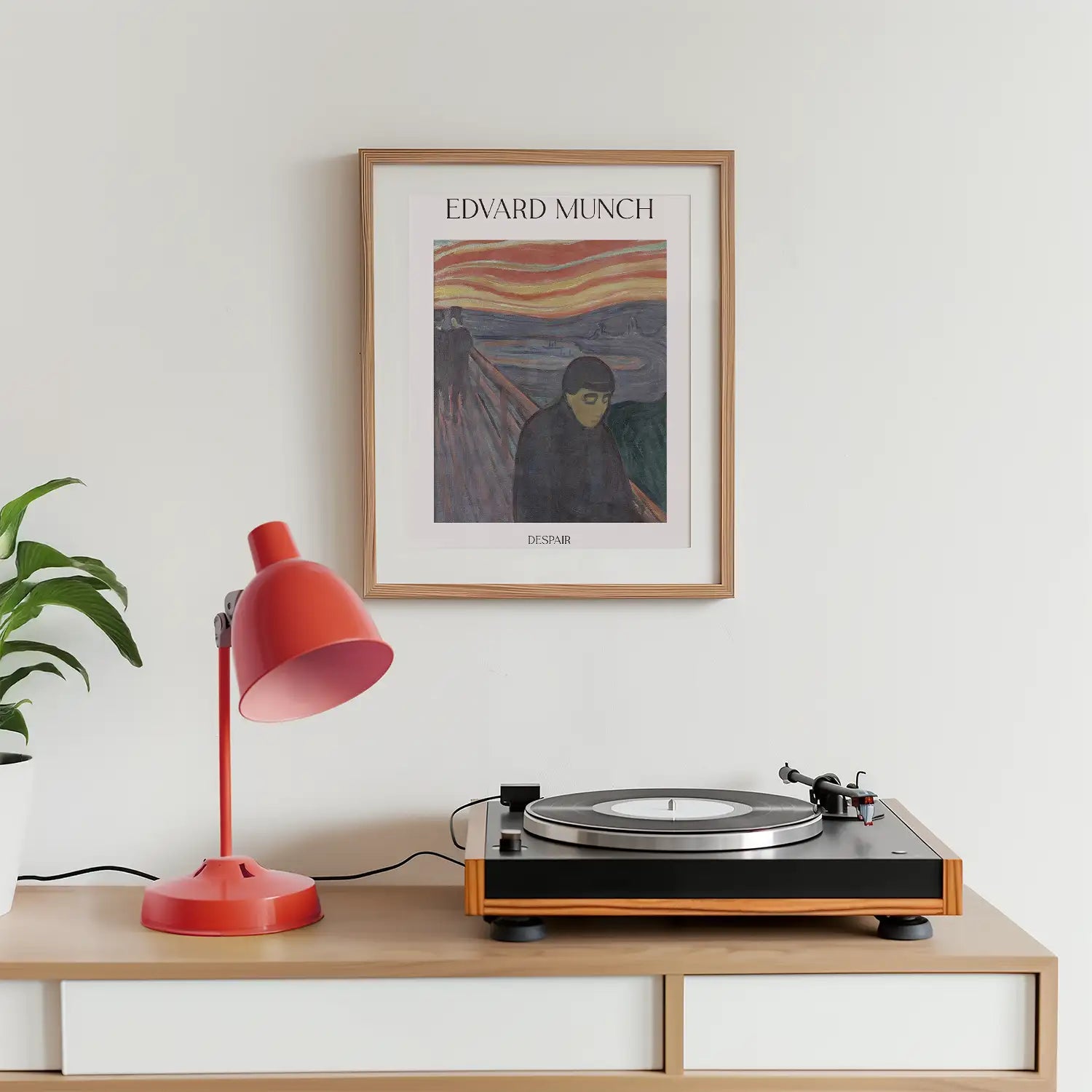 Framed poster of Edvard Munch's artwork "Despair," displayed on a wall above a turntable and a red desk lamp, with a green potted plant nearby.