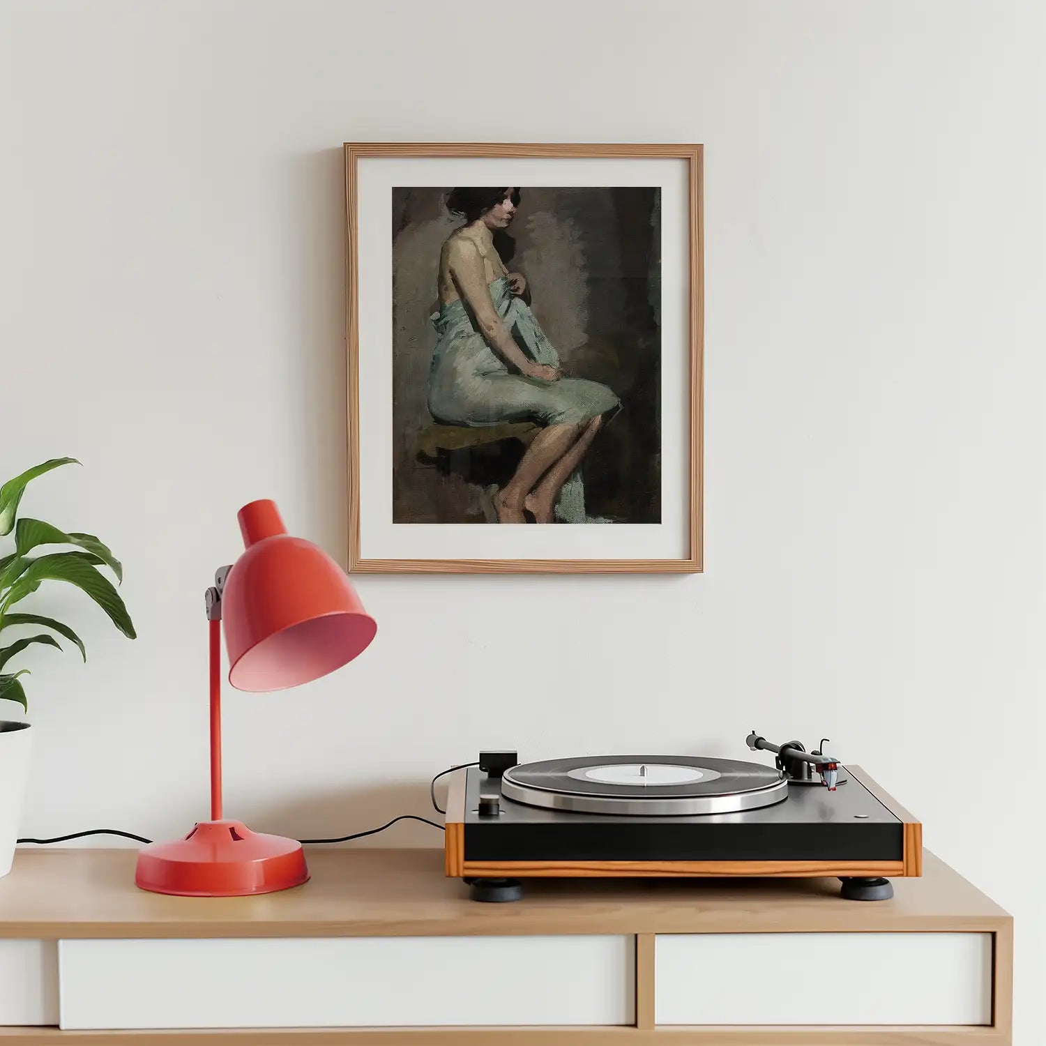 A framed painting of a seated woman in a light blue garment, displayed on a wall above a record player and a red desk lamp, with a green plant nearby.