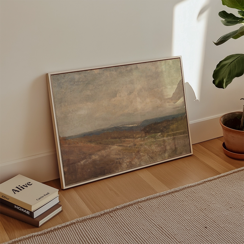 A vintage landscape painting propped against a wall next to stacked books and a potted plant in a cozy interior setting.