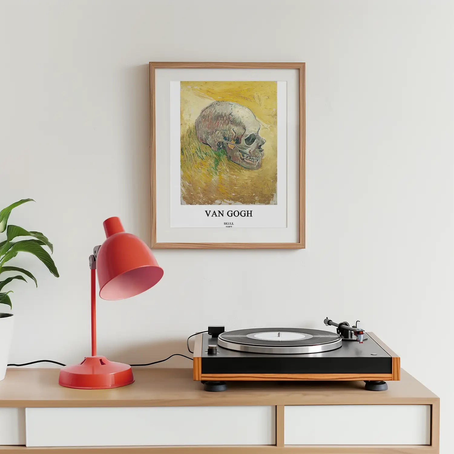 Van Gogh Skull painting framed on a wall above a turntable and a red lamp with a potted plant in the background.