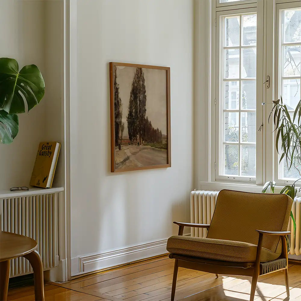 A framed painting of trees on a wall in a stylish room with a chair and a potted plant, with a book titled "Great Gatsby" visible nearby.