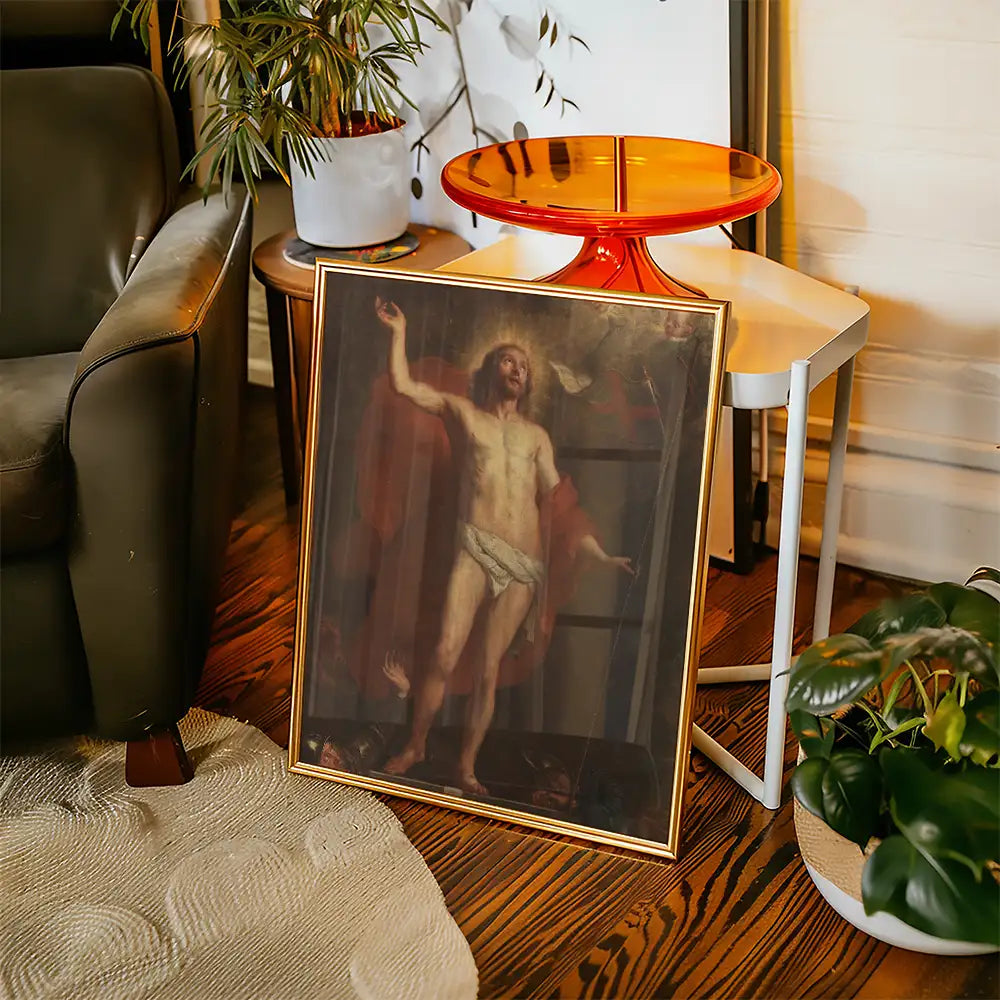 Framed religious painting of a figure in a white cloth, displayed next to a modern side table and indoor plants.