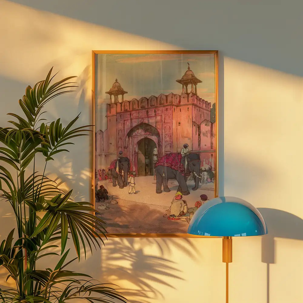 Painting of an ornate pink gate with elephants and people, framed and displayed in a modern living space with a green plant and a blue lamp.