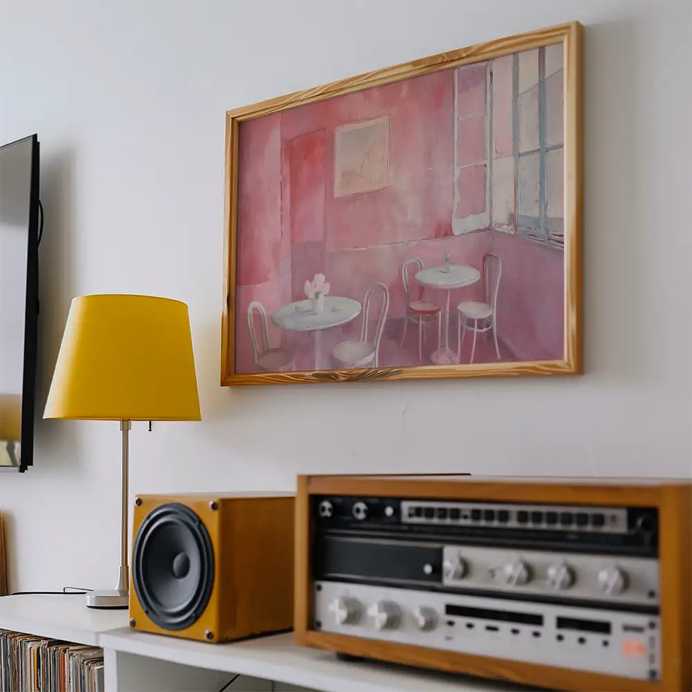 Modern reprint of a famous painting featuring a pink cafe scene with tables and chairs, framed in wood, displayed in a stylish living room setting.