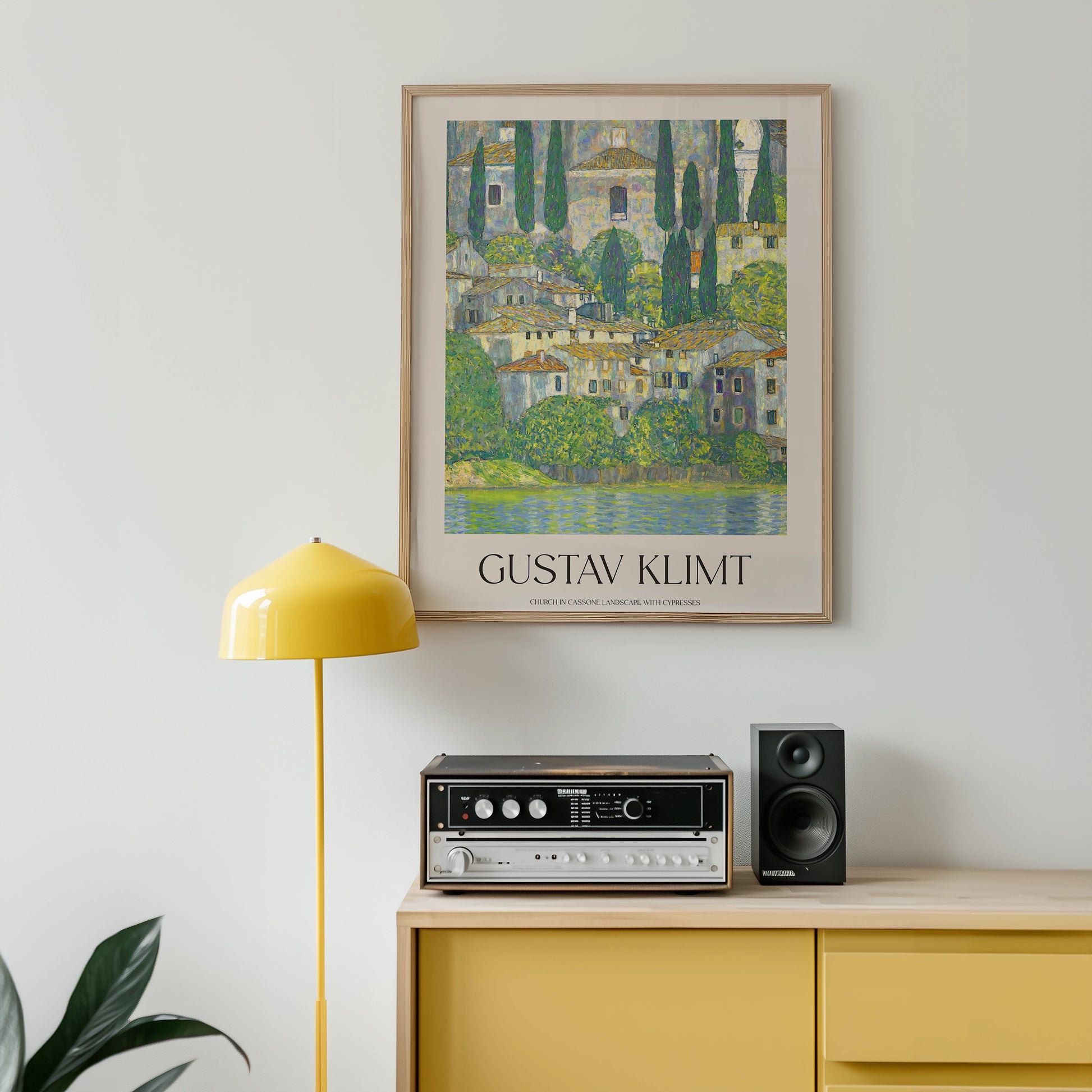 Gustav Klimt painting titled "Church in Cassone" framed and displayed on a wall above a yellow lamp and a stereo system on a wooden cabinet