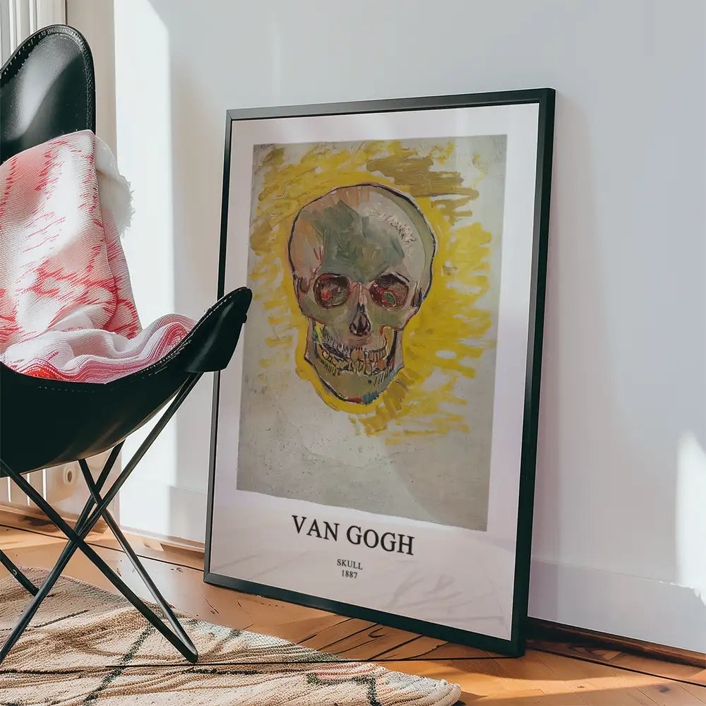 Framed poster of Van Gogh's "Skull" (1887) leaning against a wall beside a black chair and a patterned rug.