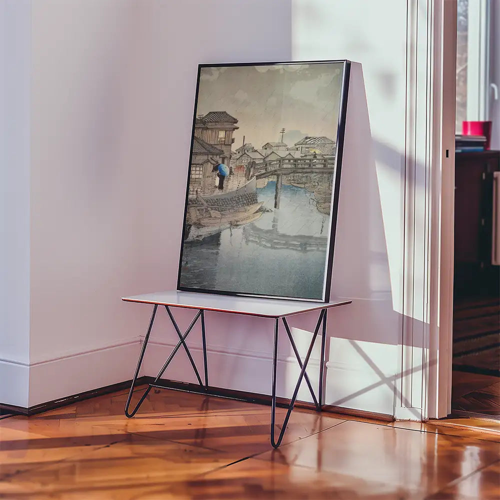 Framed painting of a serene waterway scene with traditional architecture displayed on a white table in a well-lit room.