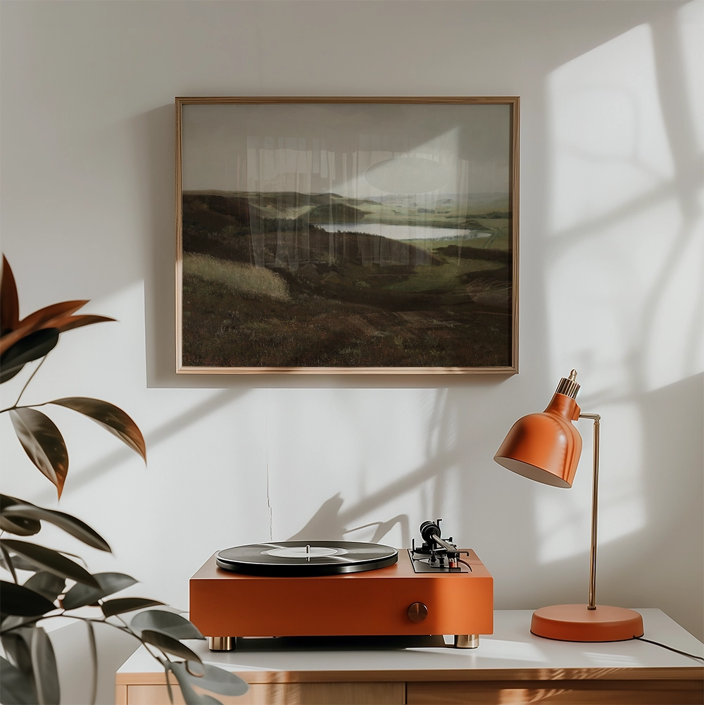 A framed landscape painting hung above a modern orange turntable and lamp in a bright, minimalist room.
