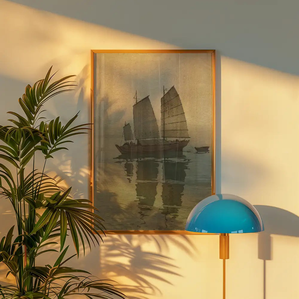 Framed painting of traditional sailing boats on calm water, with reflections, surrounded by indoor plants and a stylish lamp.