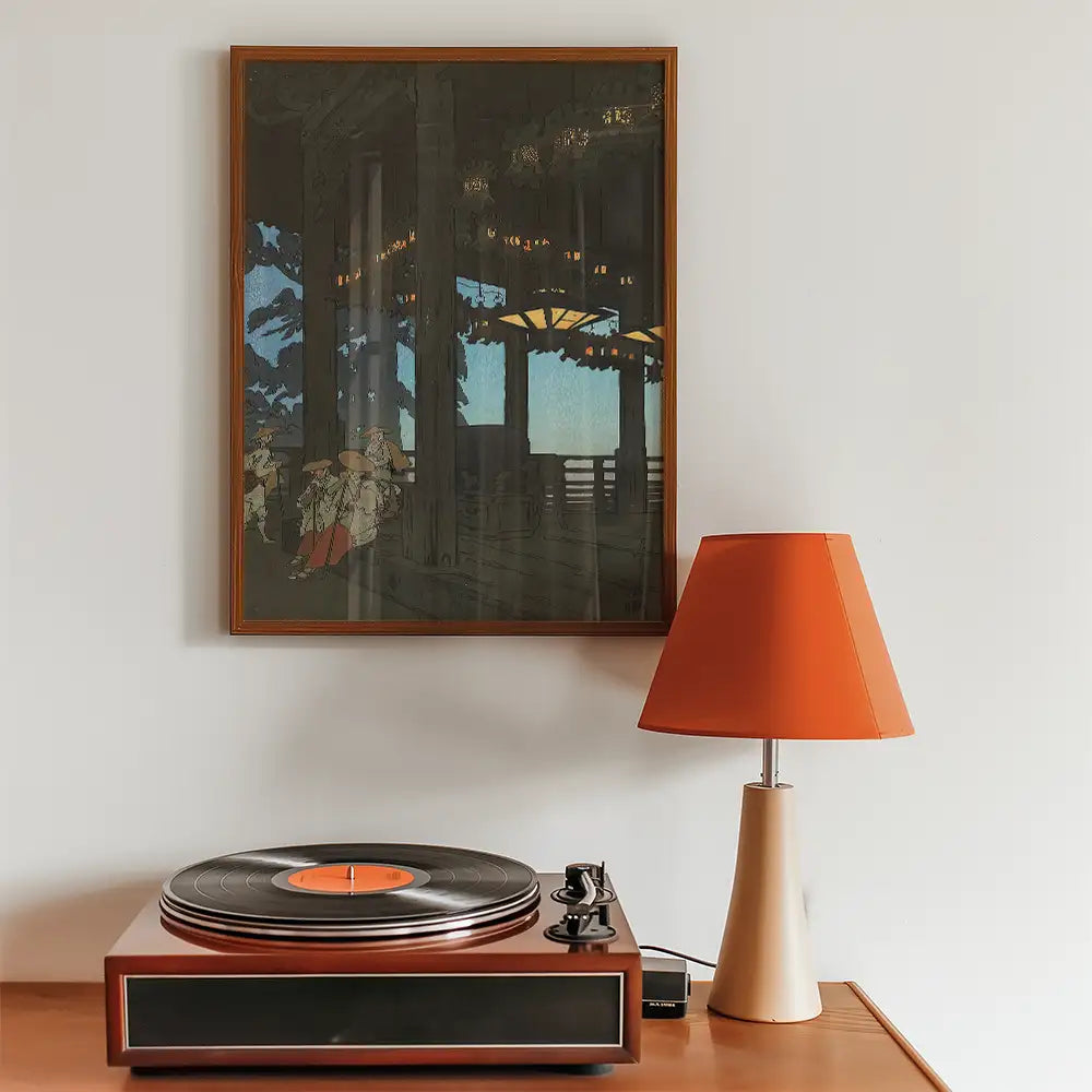 Framed painting depicting a serene indoor scene with figures, displayed above a vintage record player and a modern orange lamp.