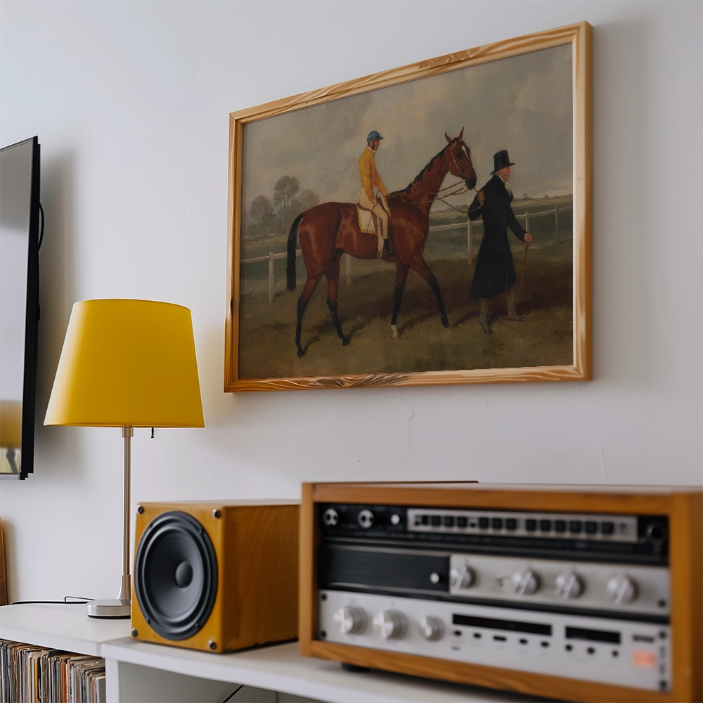 Painting of a horse being led by a man in a black coat, displayed in a wooden frame on a wall, with a yellow lamp and audio equipment nearby.