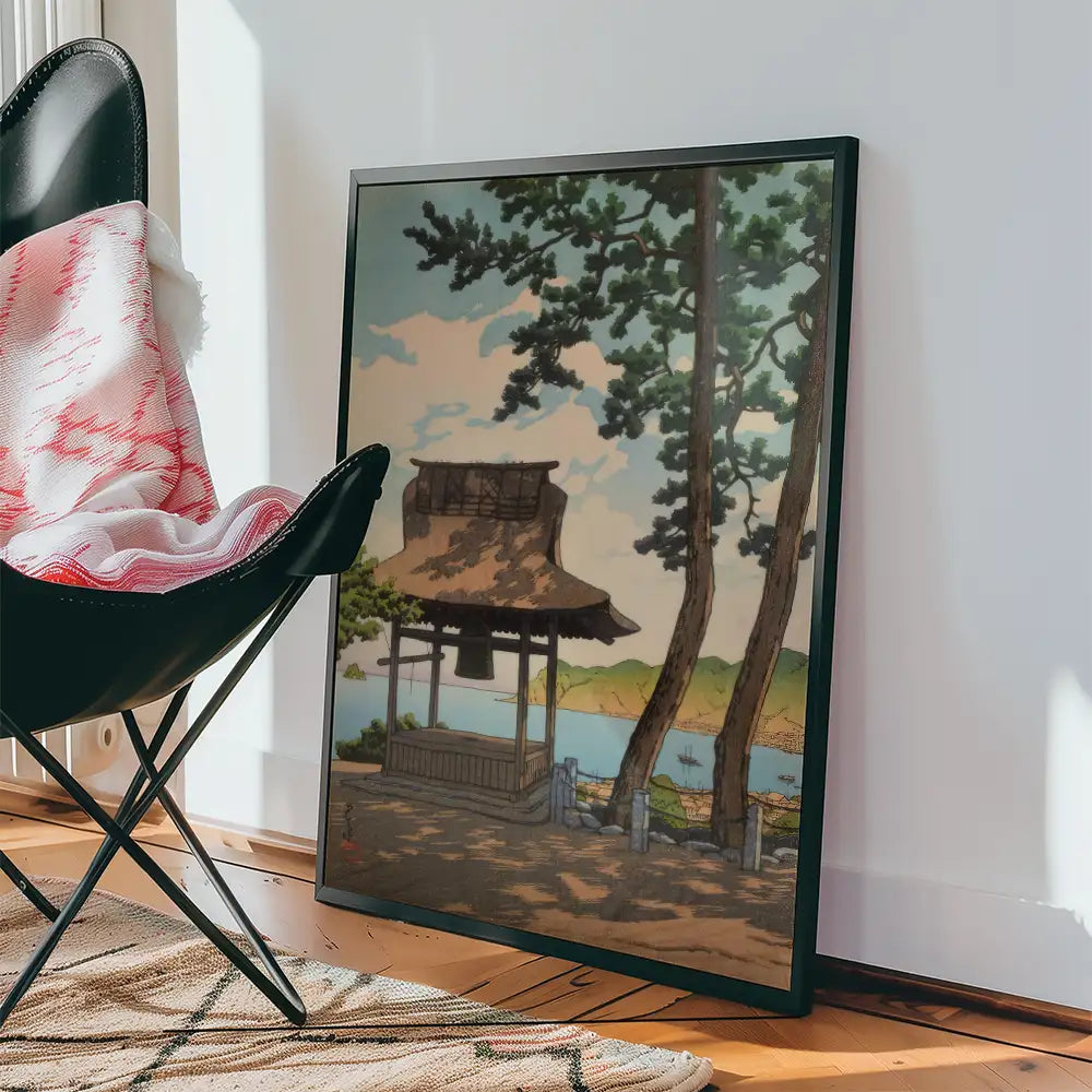 Framed painting of a serene landscape featuring a gazebo by a calm lake, surrounded by trees and distant hills, displayed next to a black chair with a red and white blanket.