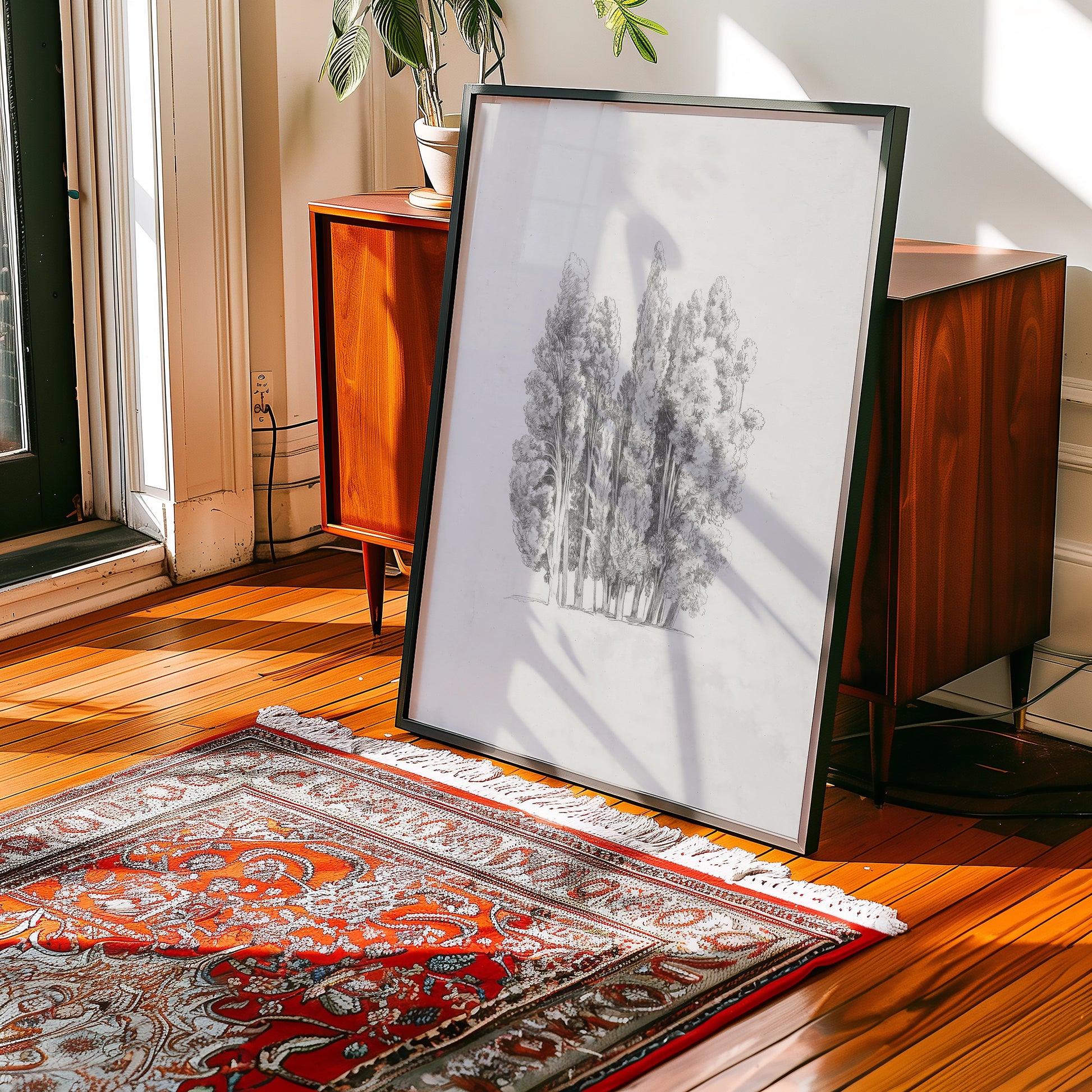 Framed black and white painting of trees leaning against a wooden cabinet on a patterned rug.