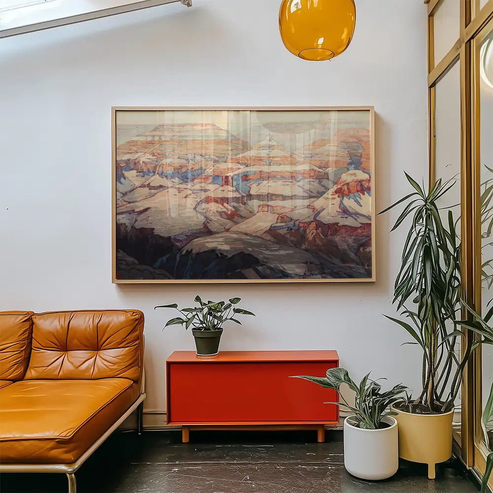 Framed landscape painting hanging on a wall above a red cabinet with indoor plants and a brown leather sofa in a modern living room setting.
